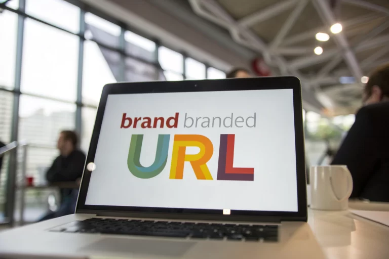 Framed digital screen showing a branded URL in vibrant colors, set in a modern office with keyboard and mouse elements.