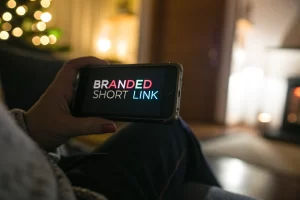 A close-up of a mobile phone screen showing a glowing branded short link in a dimly-lit room, with a blurred background and soft lighting that creates a welcoming atmosphere.